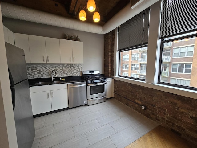 kitchen with sink, appliances with stainless steel finishes, white cabinetry, tasteful backsplash, and brick wall