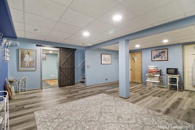 basement with hardwood / wood-style flooring, a barn door, and a paneled ceiling