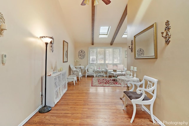 living room featuring beamed ceiling, ceiling fan, a skylight, and light hardwood / wood-style flooring