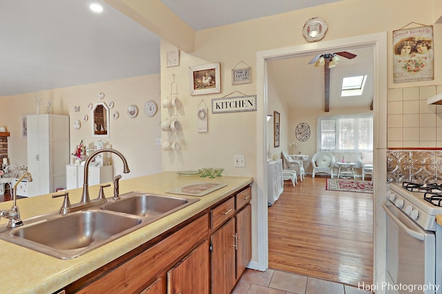 kitchen featuring light tile patterned flooring, white gas range, a skylight, and sink