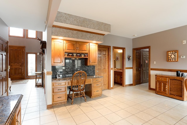 kitchen with backsplash, dark stone countertops, built in desk, and light tile patterned floors