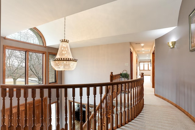 hall with a notable chandelier, vaulted ceiling, and light colored carpet