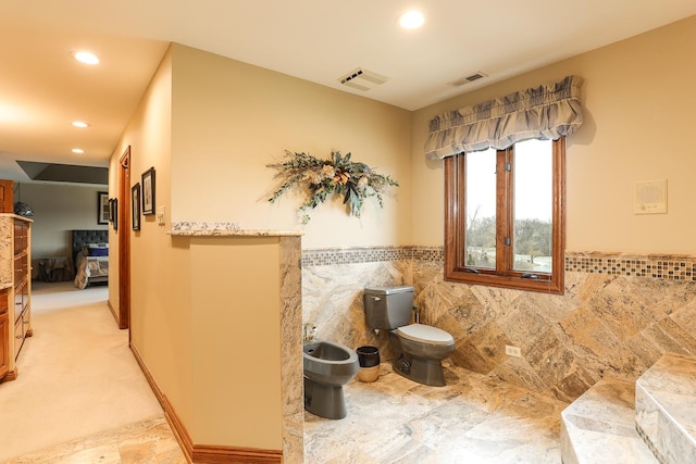 bathroom featuring toilet, tile walls, and a bidet