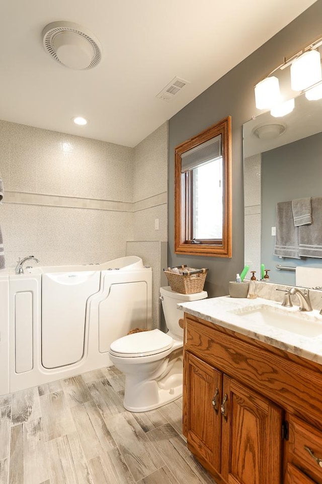 bathroom with hardwood / wood-style floors, toilet, a washtub, and vanity