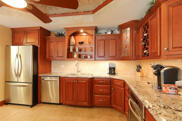 kitchen featuring appliances with stainless steel finishes, light stone counters, decorative backsplash, a tray ceiling, and sink