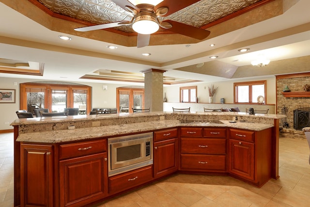 kitchen with a raised ceiling, plenty of natural light, light stone countertops, and stainless steel microwave