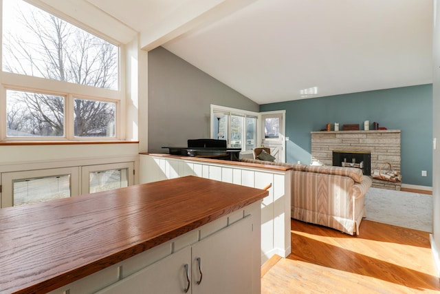 kitchen featuring wood counters, a stone fireplace, white cabinetry, high vaulted ceiling, and light hardwood / wood-style floors