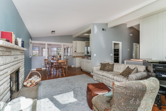 living room featuring a stone fireplace, dark wood-type flooring, and lofted ceiling with beams