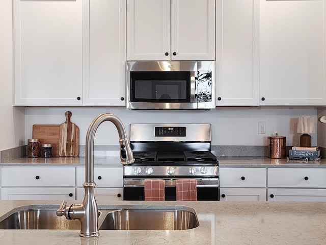 kitchen with stainless steel appliances, white cabinetry, light stone countertops, and sink