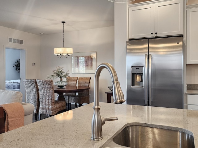 kitchen with sink, decorative light fixtures, stainless steel fridge with ice dispenser, light stone countertops, and white cabinets