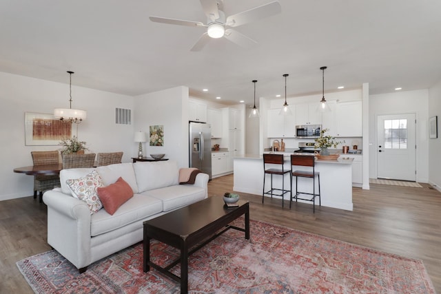 living room featuring ceiling fan with notable chandelier and light hardwood / wood-style flooring