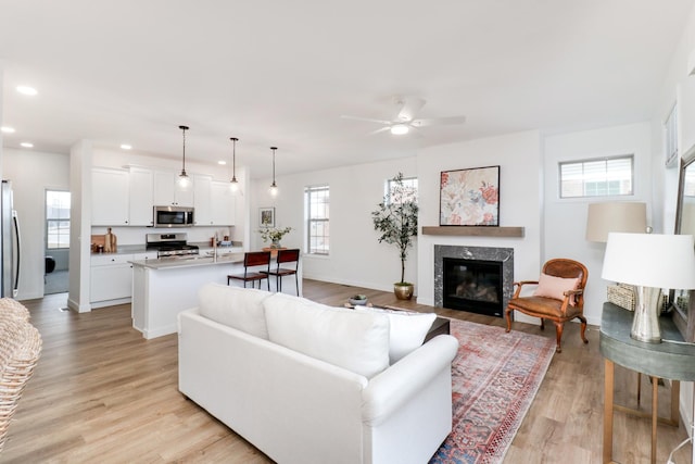 living room featuring ceiling fan, a high end fireplace, and light wood-type flooring