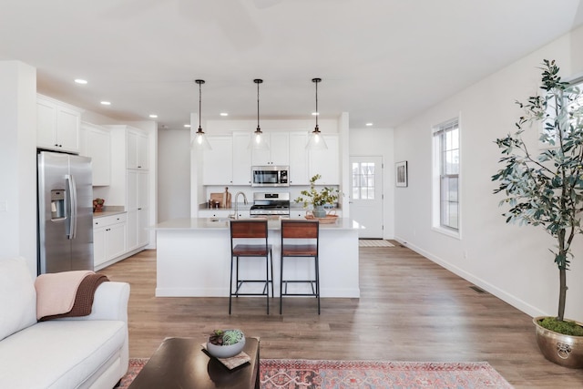 kitchen featuring hanging light fixtures, stainless steel appliances, an island with sink, and white cabinets