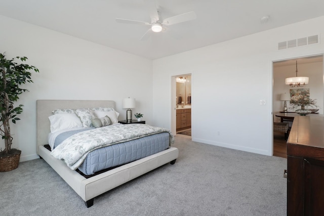 bedroom with ceiling fan with notable chandelier, light colored carpet, and ensuite bath