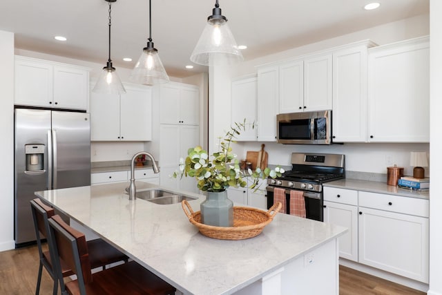 kitchen with sink, hanging light fixtures, a center island with sink, stainless steel appliances, and white cabinets