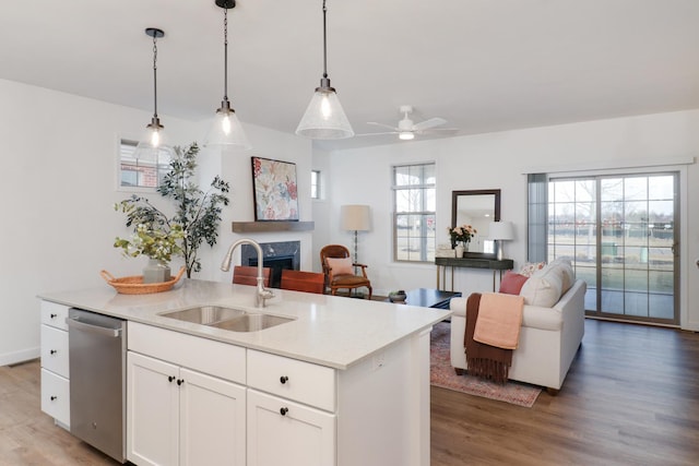 kitchen with decorative light fixtures, dishwasher, sink, white cabinets, and a center island with sink