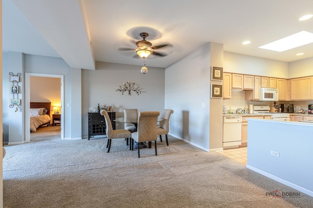 dining room featuring ceiling fan, a skylight, sink, and light carpet