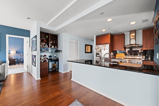 kitchen with dark wood-type flooring, stainless steel fridge, stove, kitchen peninsula, and wall chimney exhaust hood