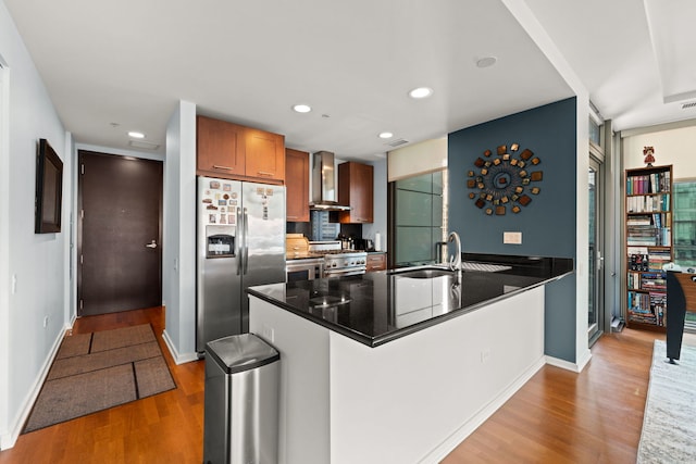 kitchen featuring sink, hardwood / wood-style flooring, appliances with stainless steel finishes, kitchen peninsula, and wall chimney exhaust hood