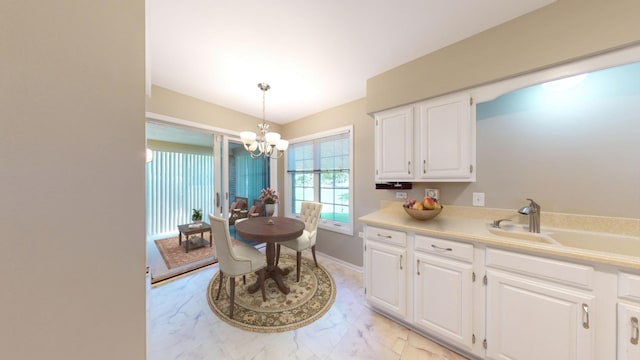 kitchen with hanging light fixtures, white cabinetry, sink, and a notable chandelier