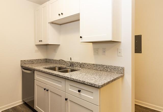 kitchen featuring white cabinetry, dishwasher, sink, light stone counters, and dark wood-type flooring