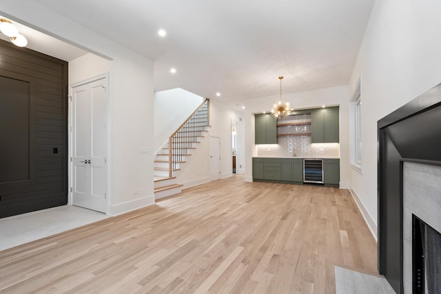 unfurnished living room featuring wine cooler, a notable chandelier, and light wood-type flooring