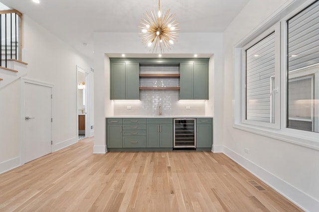 bar with tasteful backsplash, beverage cooler, green cabinets, a notable chandelier, and light wood-type flooring