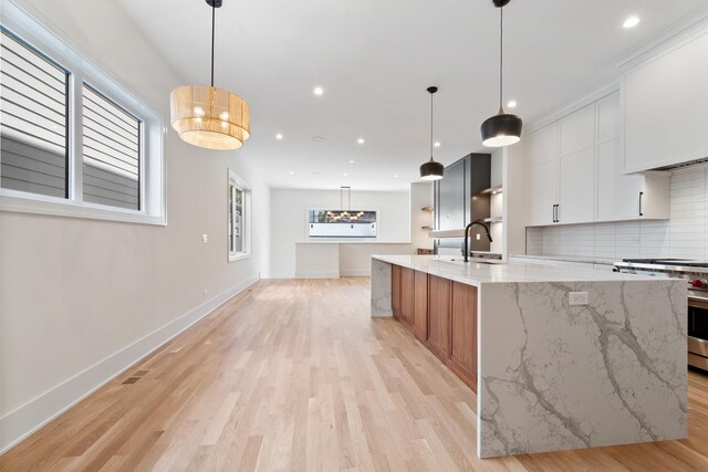 kitchen featuring a spacious island, stainless steel range oven, white cabinetry, light stone counters, and pendant lighting