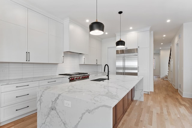 kitchen featuring white cabinetry, high end appliances, hanging light fixtures, and a kitchen island with sink