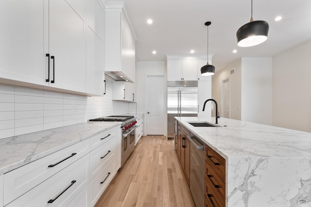 kitchen with sink, white cabinetry, hanging light fixtures, high end appliances, and light stone counters