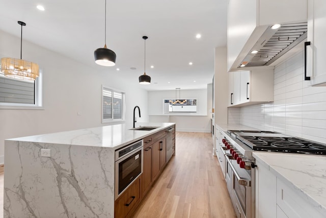 kitchen featuring sink, light stone counters, hanging light fixtures, white cabinets, and wall chimney range hood