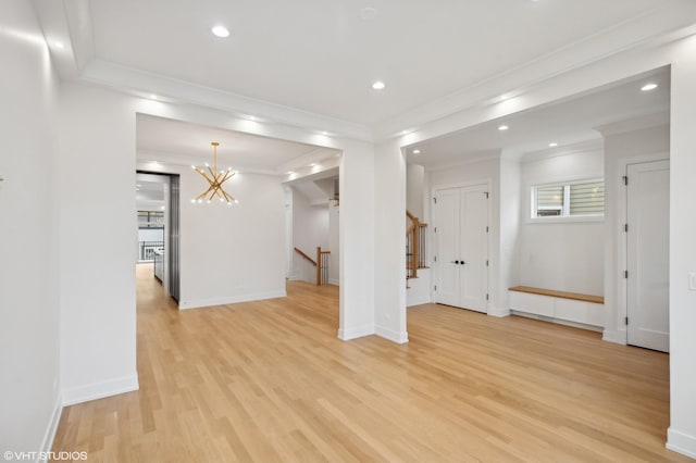 unfurnished living room with an inviting chandelier, ornamental molding, and light wood-type flooring