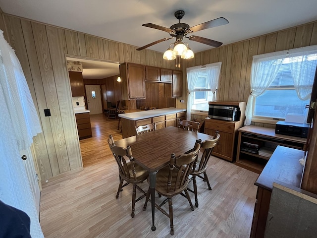 dining space featuring ceiling fan, wooden walls, and light hardwood / wood-style flooring