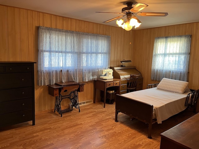 bedroom featuring multiple windows, wooden walls, and light hardwood / wood-style flooring