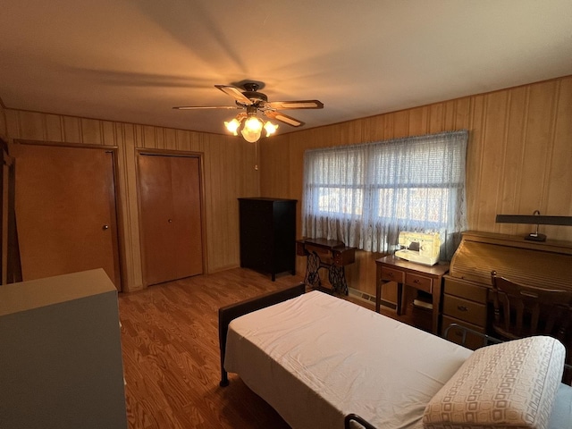 bedroom with multiple closets, ceiling fan, wood-type flooring, and wood walls