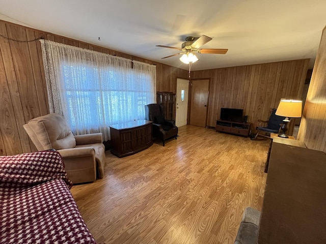 living room with ceiling fan, light wood-type flooring, and wood walls