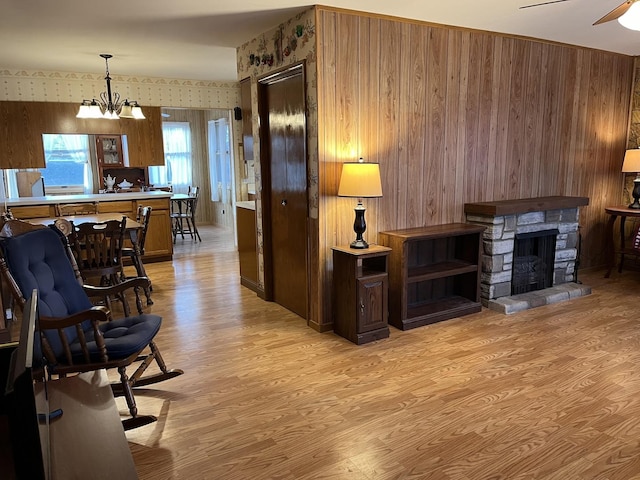 living room featuring a stone fireplace, light hardwood / wood-style flooring, and ceiling fan with notable chandelier