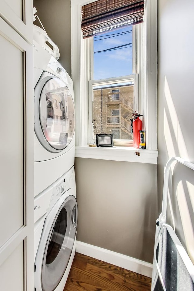 washroom with stacked washer / drying machine and dark hardwood / wood-style flooring