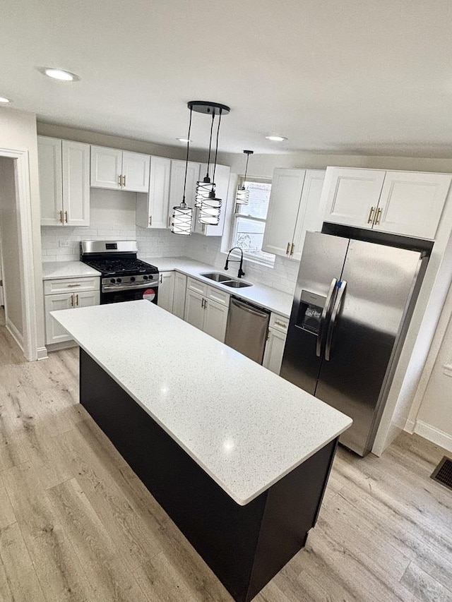 kitchen with sink, a kitchen island, pendant lighting, stainless steel appliances, and white cabinets