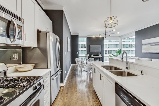 kitchen featuring sink, appliances with stainless steel finishes, hanging light fixtures, a wealth of natural light, and white cabinets