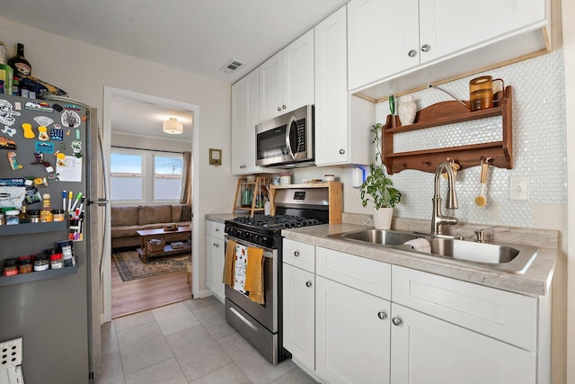 kitchen featuring sink, light tile patterned floors, white cabinetry, backsplash, and stainless steel appliances