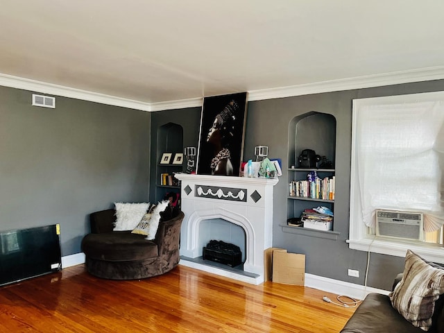 living room with wood-type flooring, ornamental molding, cooling unit, and built in shelves