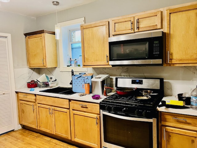 kitchen featuring pendant lighting, sink, light hardwood / wood-style flooring, stainless steel appliances, and tasteful backsplash