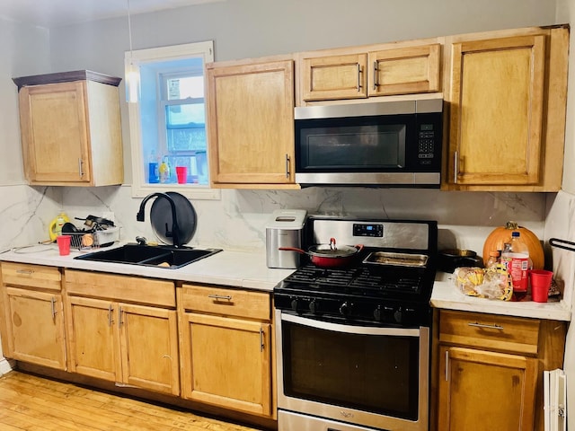 kitchen with sink, appliances with stainless steel finishes, tasteful backsplash, light brown cabinetry, and light wood-type flooring