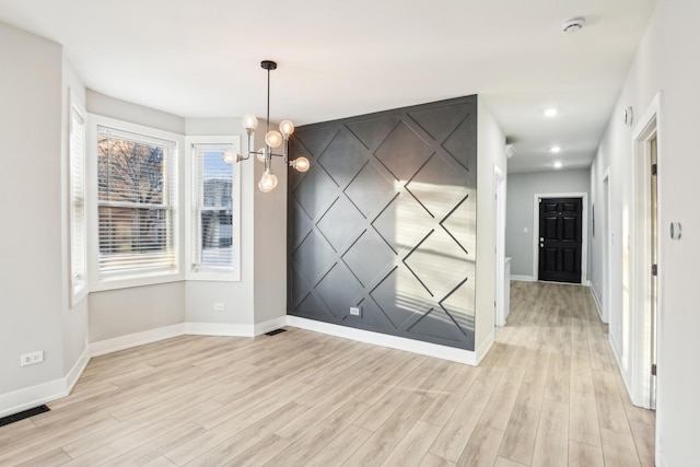 unfurnished dining area featuring a chandelier, light wood finished floors, and baseboards