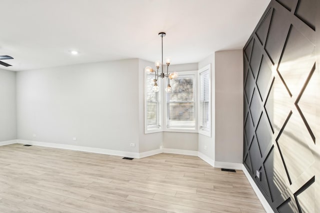 unfurnished dining area with ceiling fan with notable chandelier, light wood finished floors, visible vents, and baseboards