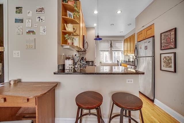 kitchen featuring appliances with stainless steel finishes, pendant lighting, a breakfast bar area, dark stone counters, and kitchen peninsula