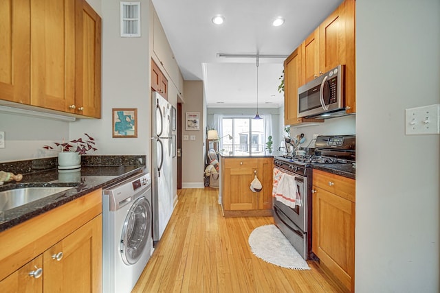 kitchen with appliances with stainless steel finishes, dark stone countertops, light hardwood / wood-style floors, washer / clothes dryer, and decorative light fixtures