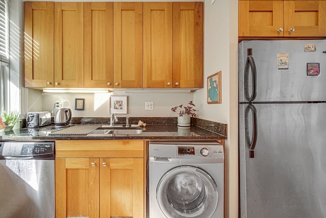 kitchen with dark stone countertops, washer / clothes dryer, sink, and appliances with stainless steel finishes