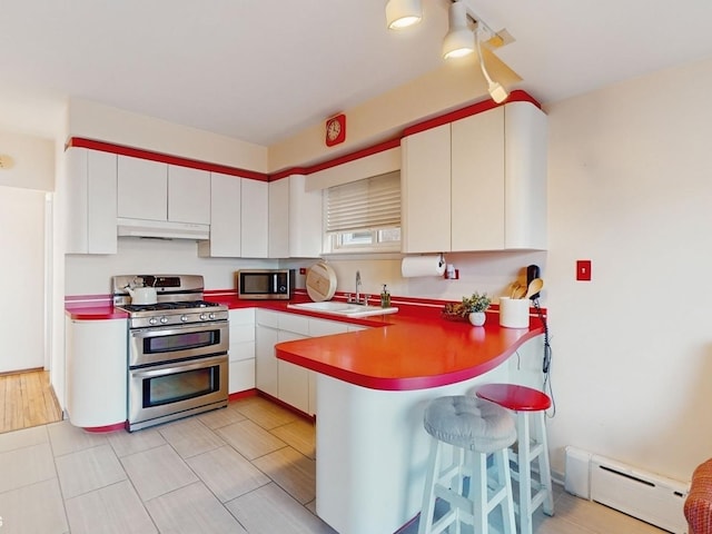 kitchen with stainless steel appliances, sink, white cabinets, and baseboard heating